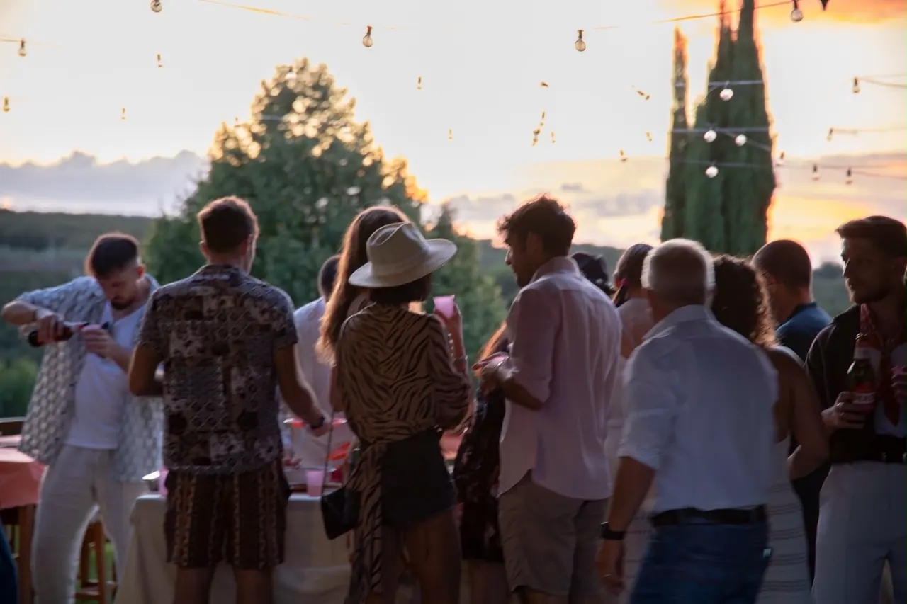 Ospiti riuniti sul prato dell'Oasi del Verde al tramonto, fra i cipressi e le luci sospese