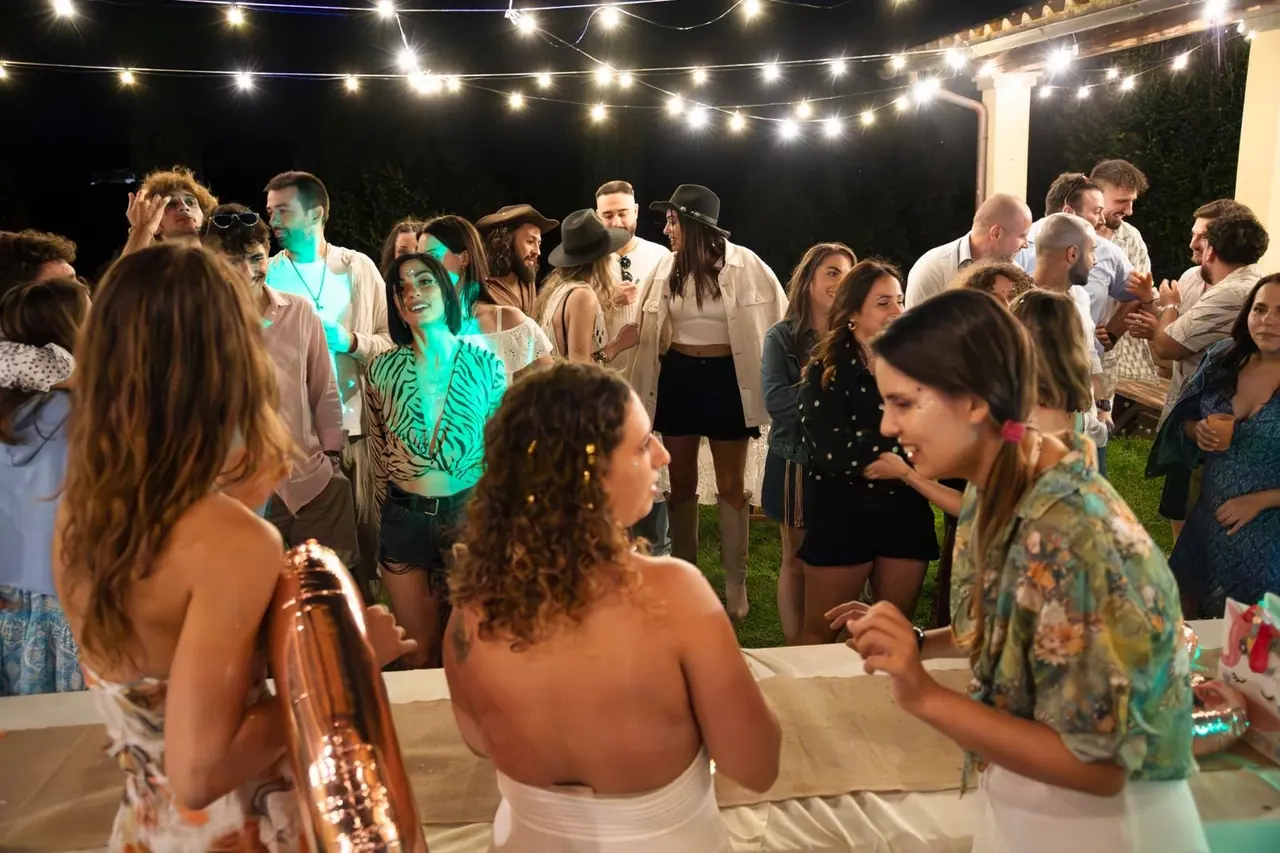 Ospiti di una festa nel giardino dell'Oasi del Verde, la sera, sotto le luci sospese