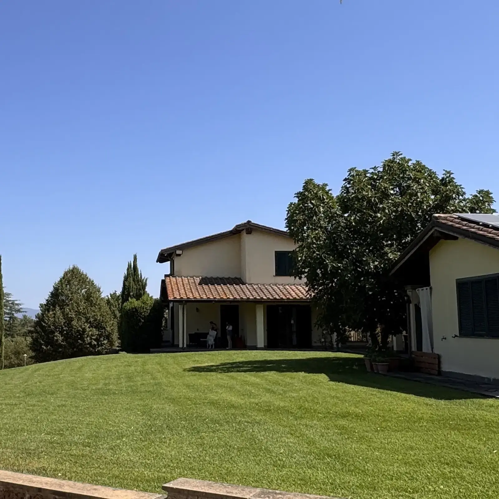 La casa dell'Oasi del Verde vista dal grande prato, con il porticato in ombra e i cipressi