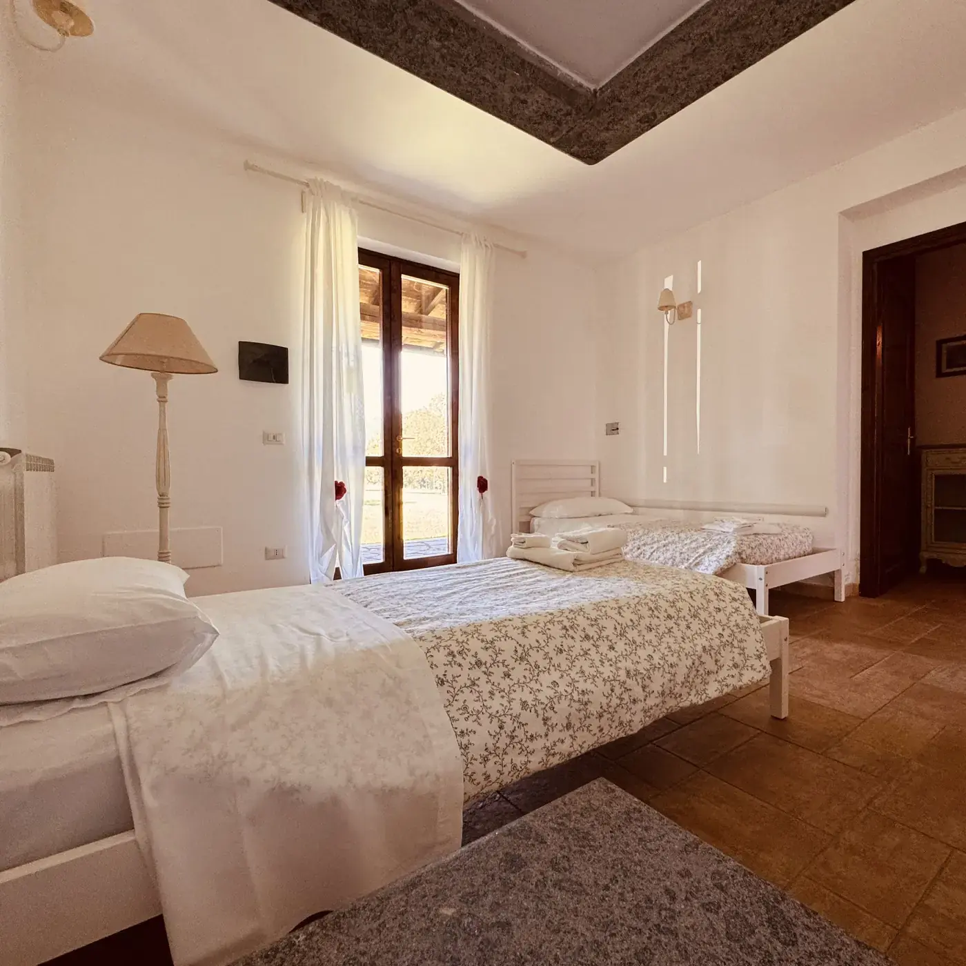 Camera dell'Oasi del Verde con letto matrimoniale e letto singolo, tende bianche e portafinestra sul giardino
